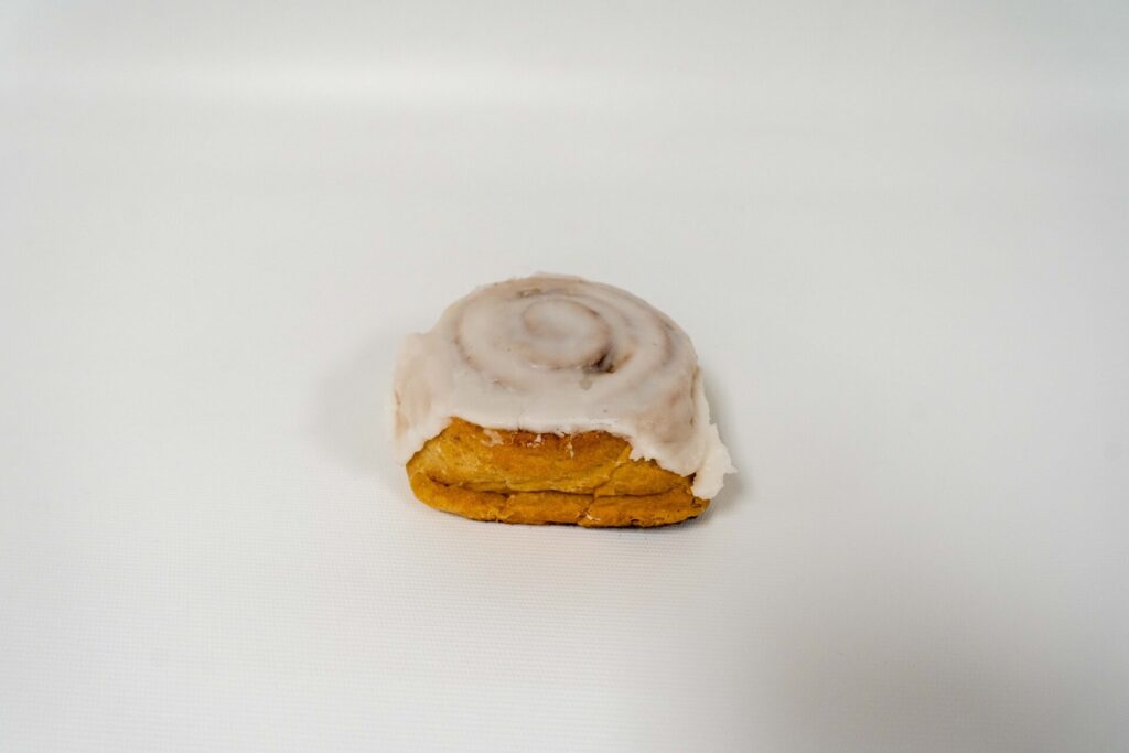 Gluten-Free White Frosted Cinnamon Roll with swirls of cinnamon and a thick layer of creamy vanilla frosting on top.