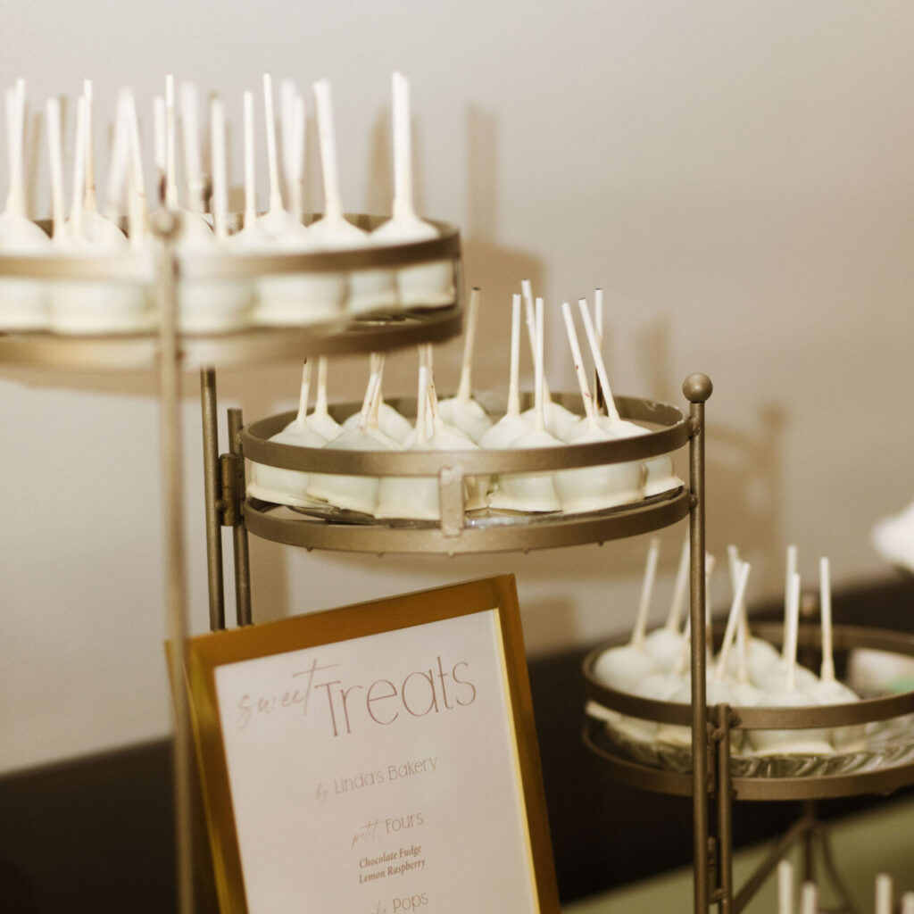White cake pops neatly arranged with visible flavor signage, featuring smooth white coating and decorative sprinkles.